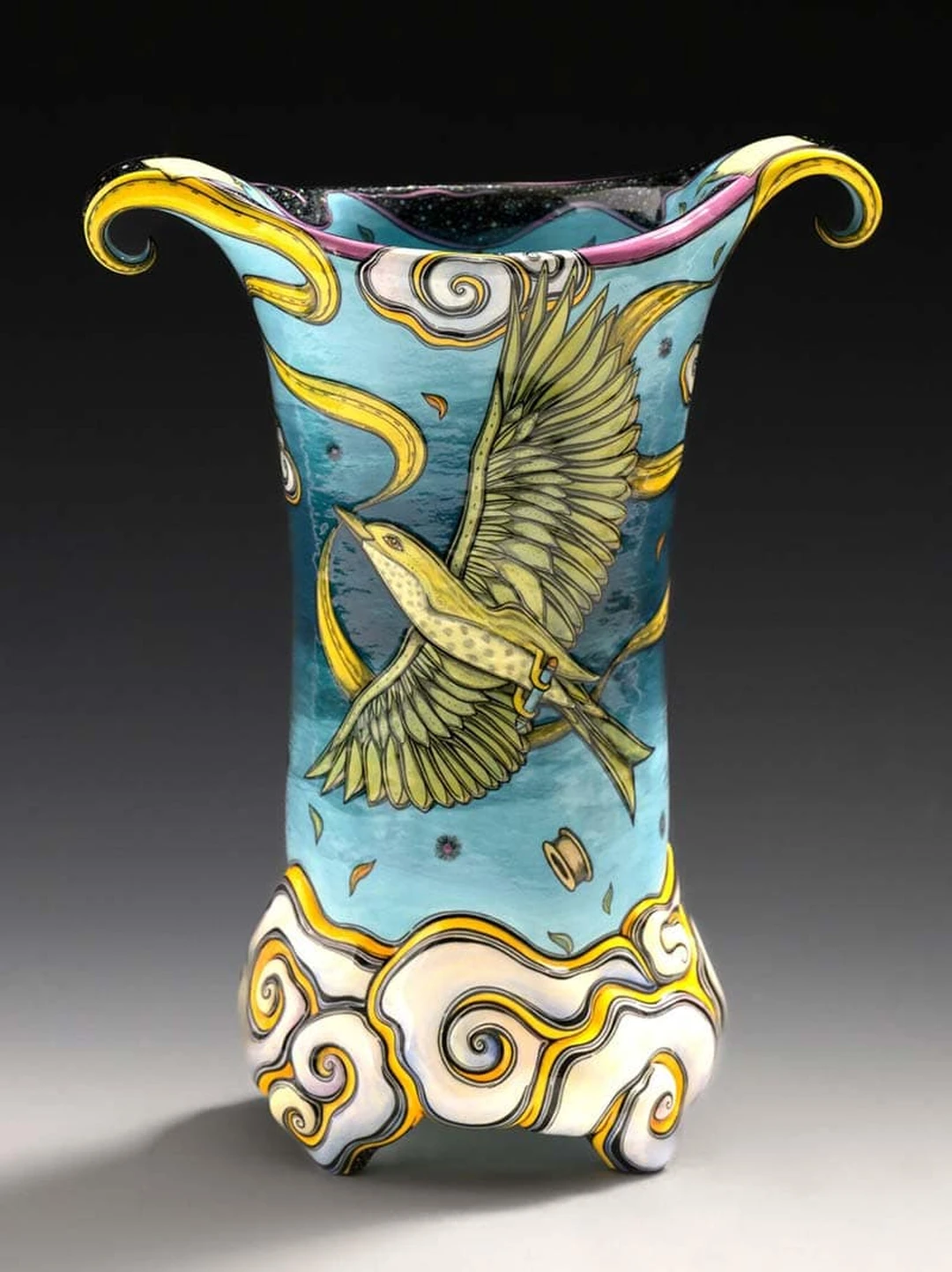 A ceramic vessel by Terri Kern, painted with a bird in flight among stylized clouds in blue, yellow and white.
