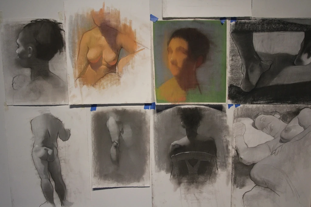 Studio wall with eight figure studies in charcoal and pastel pinned with blue tape. Tyler Wilkinson, studio view, 2013. Image from Manifest Gallery.