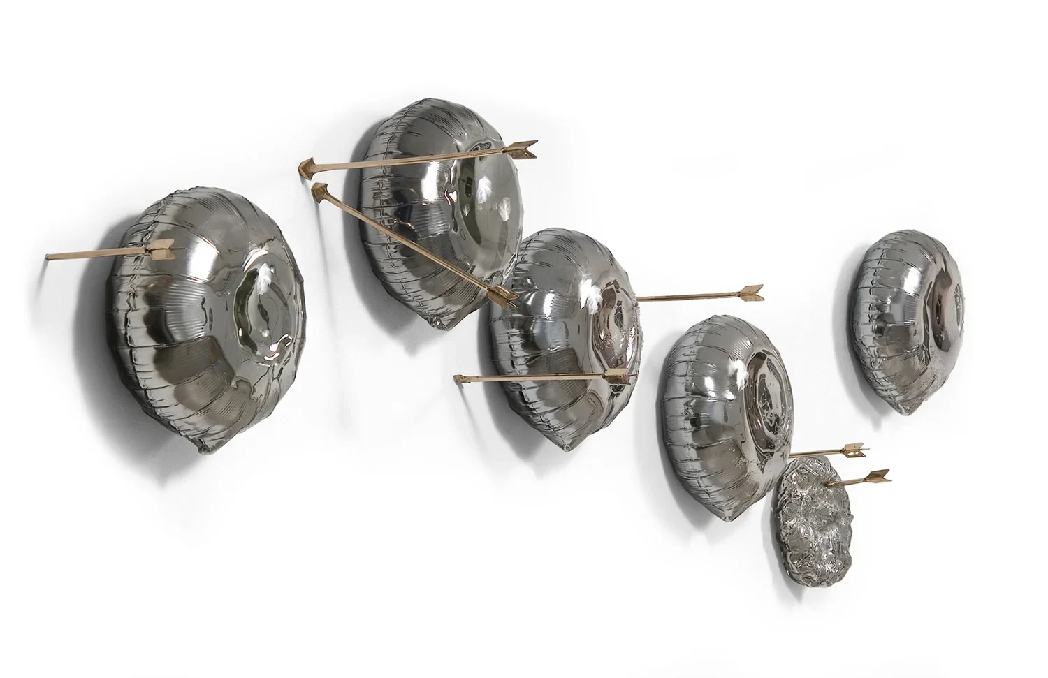 Six mirrored balloon-like glass forms floating on a white wall, pierced by long golden arrows.