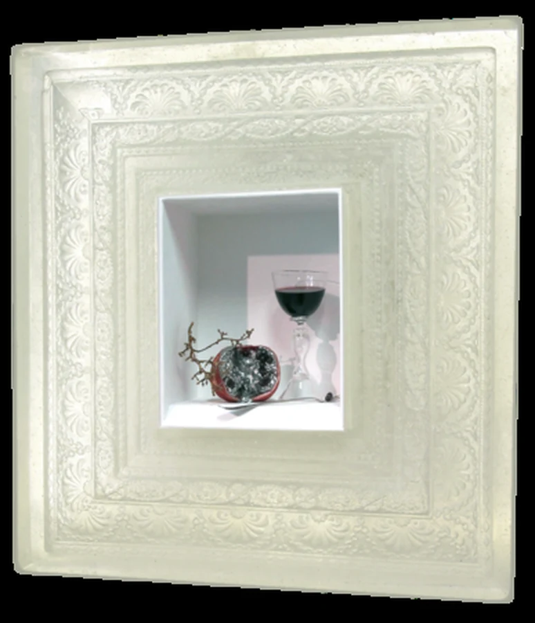An ornate white glass frame with a recessed niche holding a pomegranate, a wine glass and a dry stem.