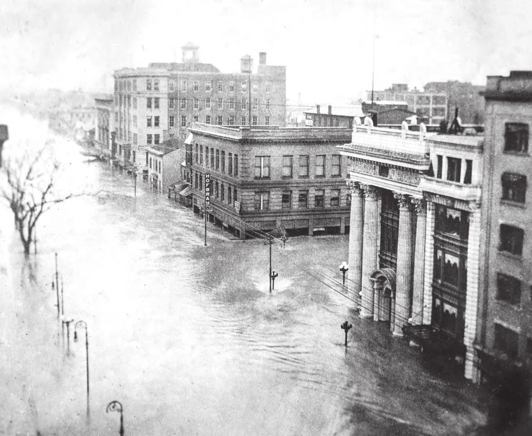 Flooded street with a columned newspaper building on the right, water covering the roadway. Image from A Flood of Memories (Miami Conservancy District, 2013).