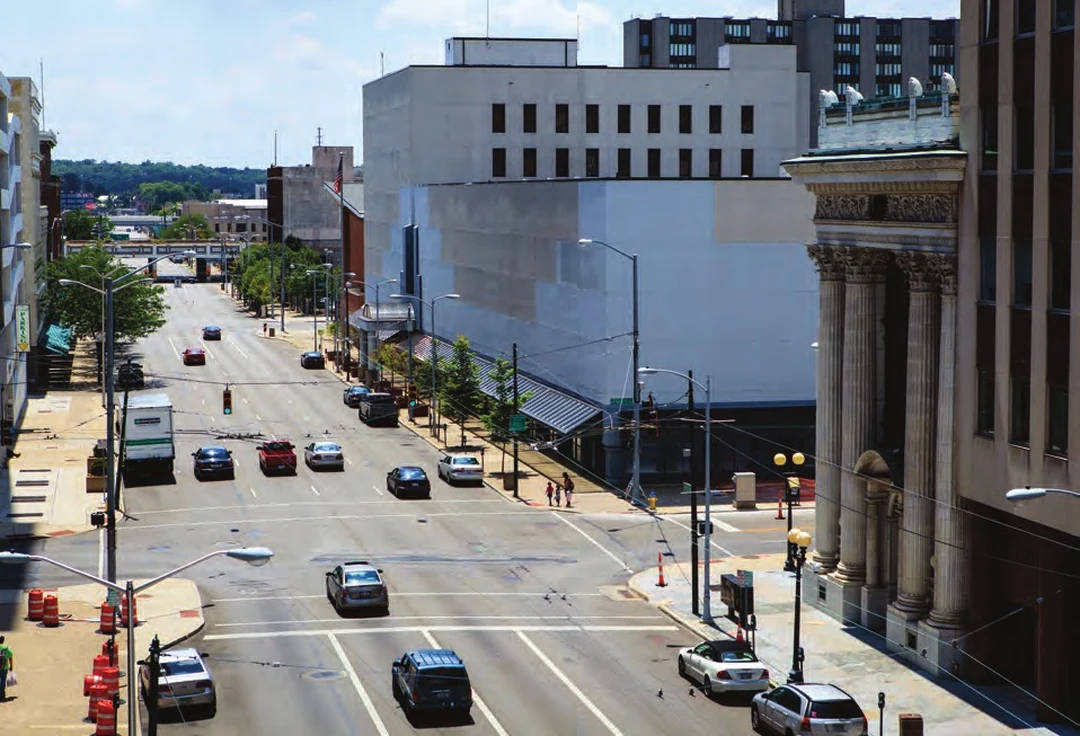 Ludlow Street in Dayton with the white Dayton Public Schools building on the left, cars on the road, and the columned Dayton Daily News building on the right. Photograph by Andy Snow. Image from A Flood of Memories, 2013.