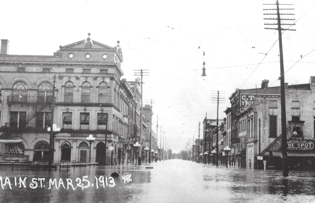 Main Street in Dayton flooded during the 1913 flood, buildings on both sides, 'Main St. Mar. 25. 1913' painted on the photograph. Image from A Flood of Memories, 2013. (Related image located during this archive's reconstruction.)