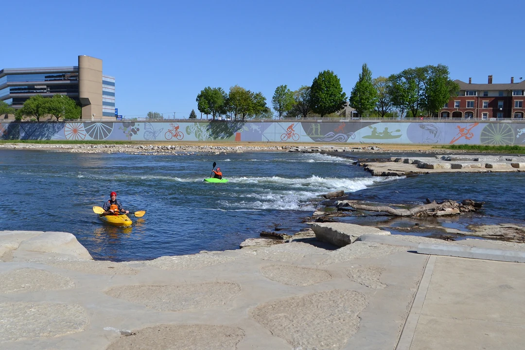 Two kayakers on the whitewater features of the RiverScape River Run in downtown Dayton; the colorful River Run mural on the floodwall behind them. Five Rivers MetroParks, 2017. (Related image located during this archive's reconstruction.)