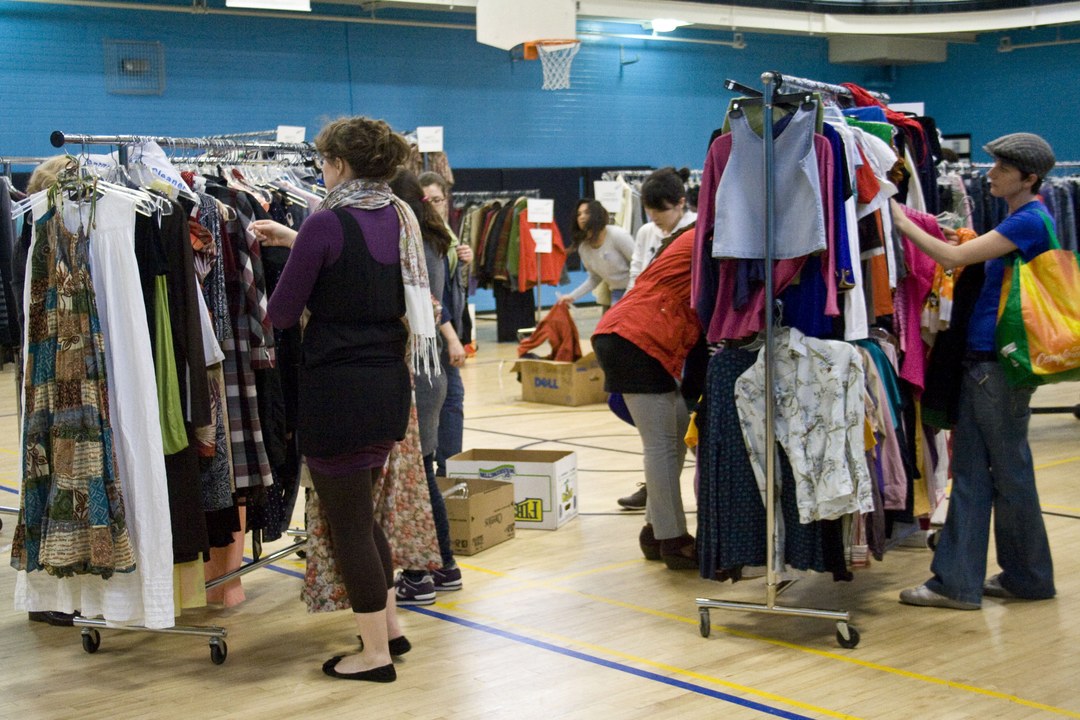 People browsing racks of secondhand clothing at a clothes swap event in a gymnasium.