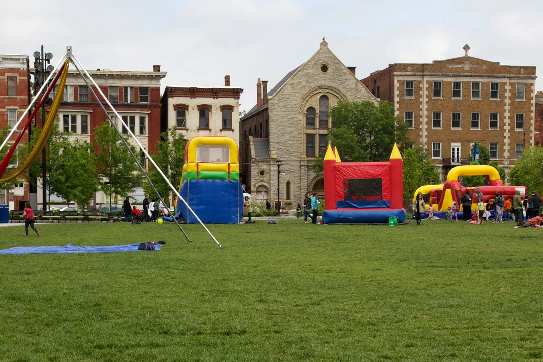 Families and colorful inflatable play structures on the lawn of Washington Park in Cincinnati, with historic buildings behind.