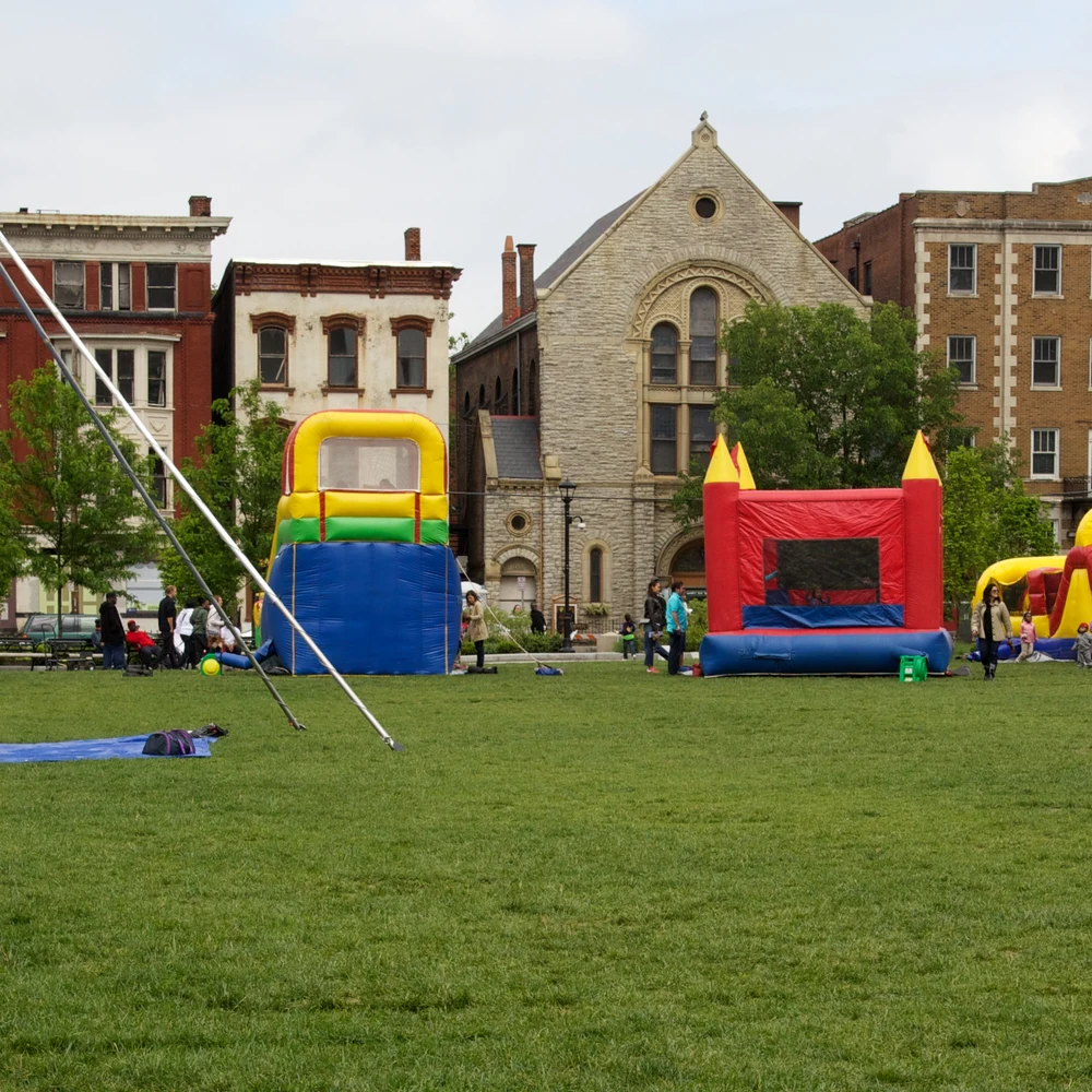 Families and colorful inflatable play structures on the lawn of Washington Park in Cincinnati, with historic buildings behind.