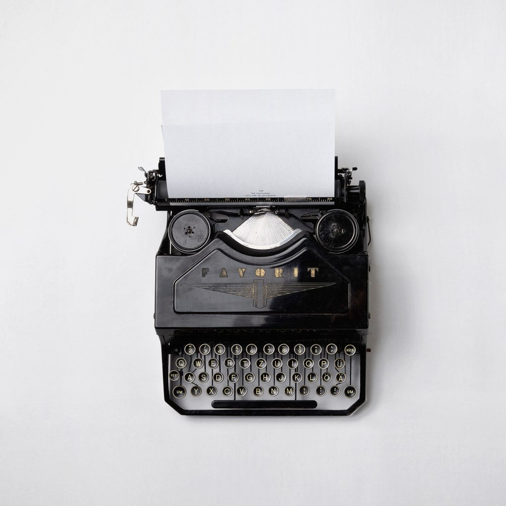 A vintage black typewriter with a blank sheet of paper, viewed from above.