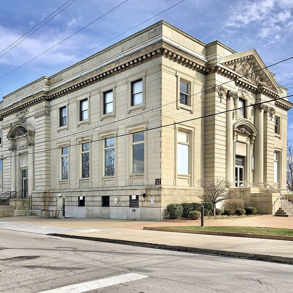 Corner view of The Carnegie in Covington, Kentucky: a Beaux-Arts stone building with rows of tall windows under a blue sky.