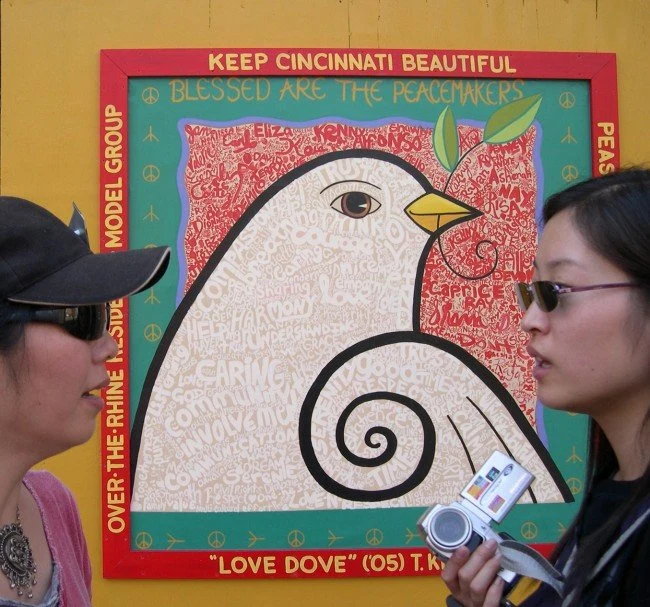 Vine Street Murals and Can-paign, mural painting by Jan Brown Checco: colorful Love Dove mural on a yellow wall, flanked by two women