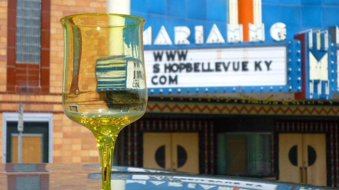 A yellow wine glass in the foreground with the marquee of the Marianne theater in Bellevue, Kentucky, behind it.
