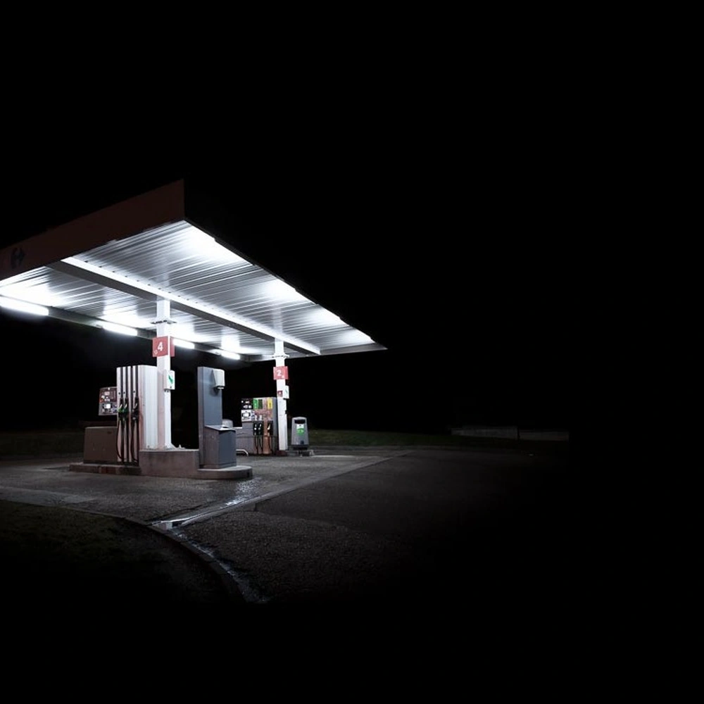 Night photograph of a brightly lit gas station beneath a vast black sky, from Xavier Blondeau's 'Presence Obscure' series.