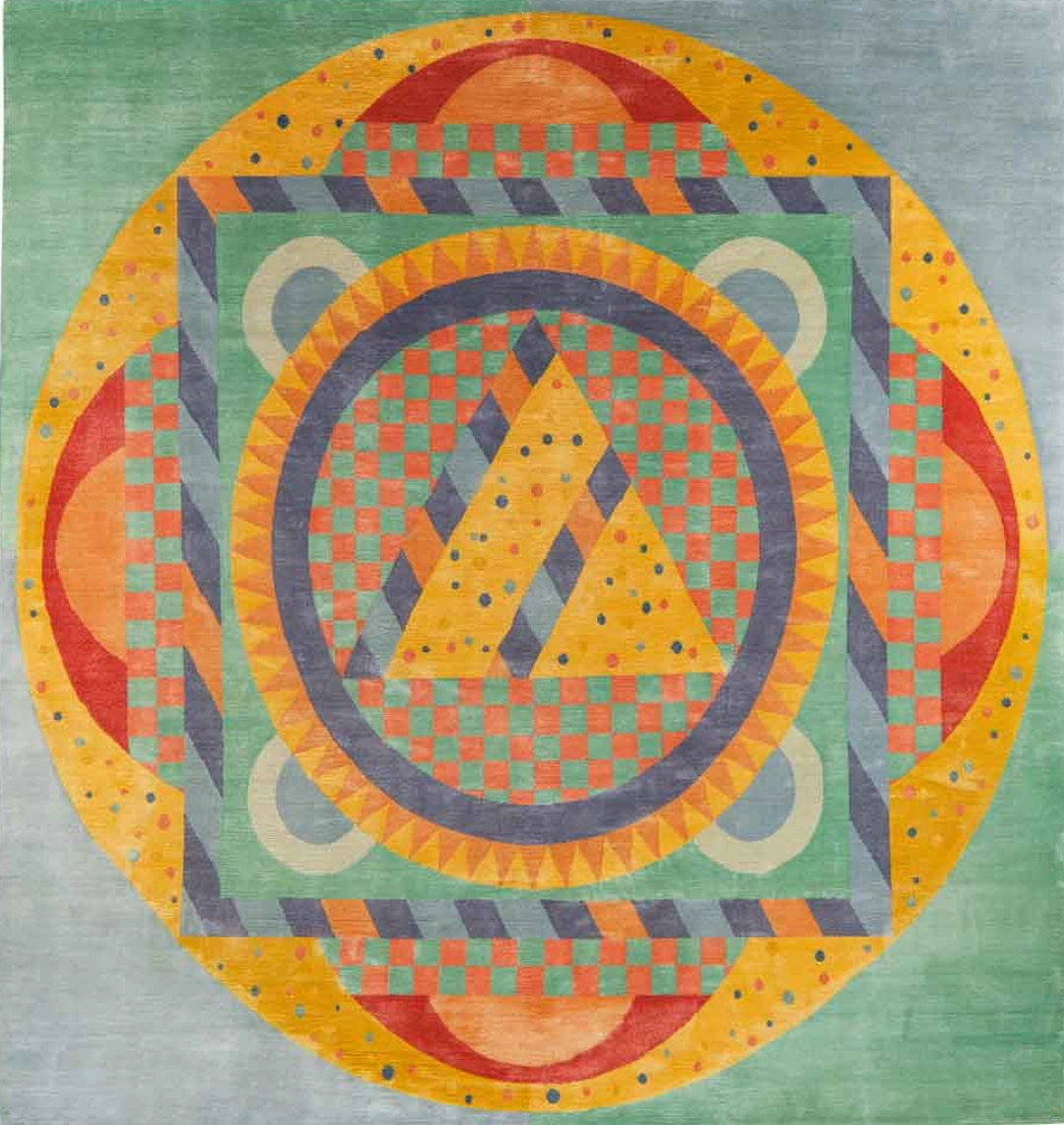 Circular mandala rug in concentric rings of yellow, orange, red and green with circles, squares and triangles on a pale green ground.