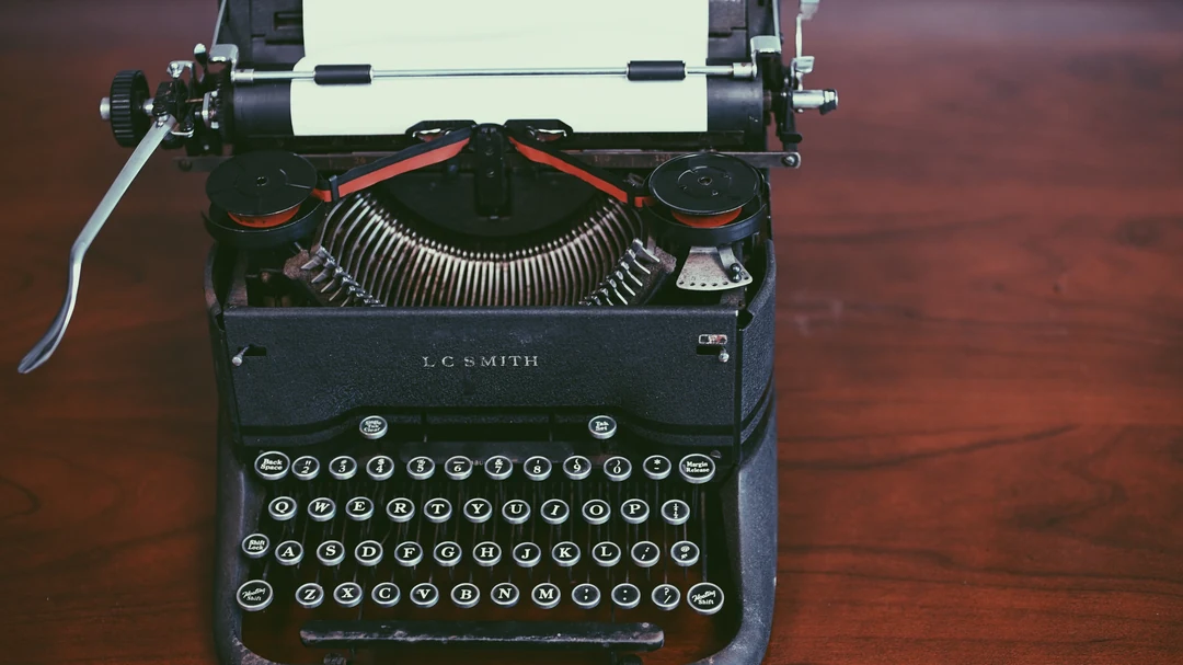 Black vintage L.C. Smith typewriter with a blank sheet of white paper in the roller and a red-and-black ribbon, round QWERTY keys.