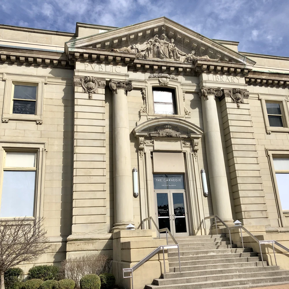 Front entrance of The Carnegie in Covington, Kentucky: a stone Beaux-Arts facade with columns, a carved pediment reading PUBLIC LIBRARY, and a glass door marked THE CARNEGIE.