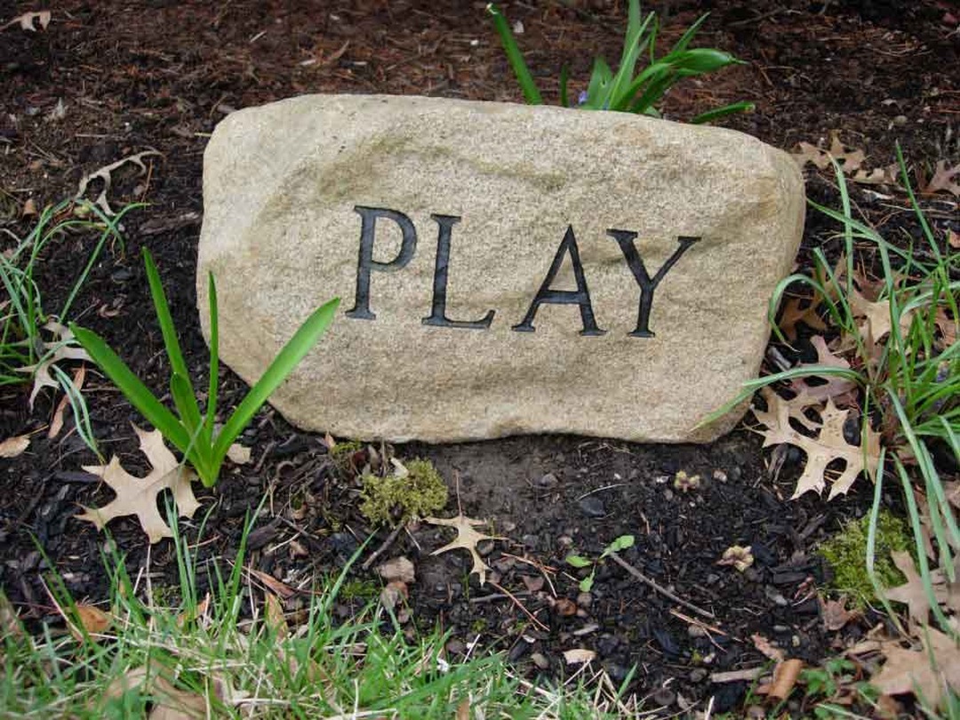 The word 'PLAY' carved into a garden stone, one of Gary Gaffney's public art messages