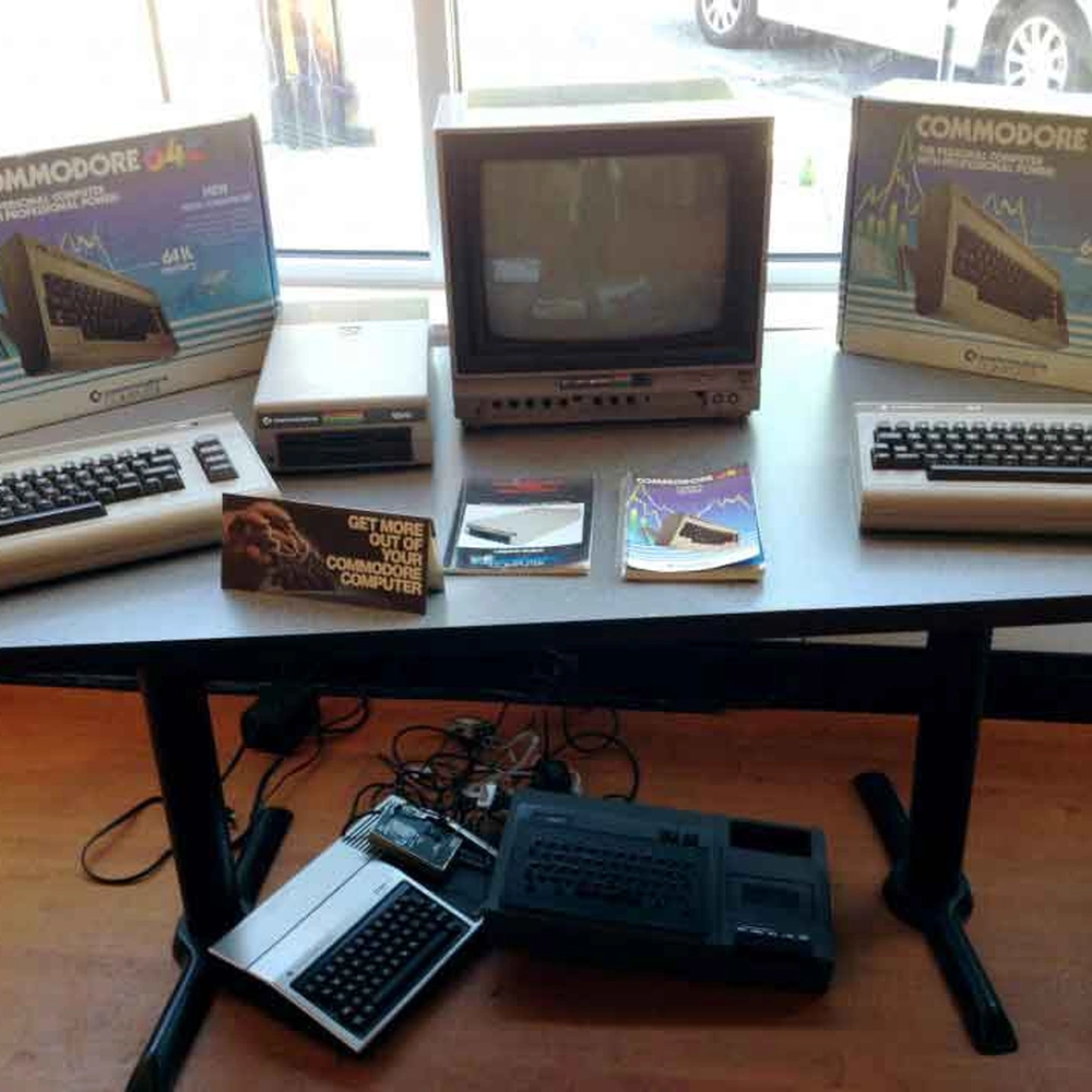 Vintage Commodore 64 computers, keyboards and monitor displayed on a table in a gallery.