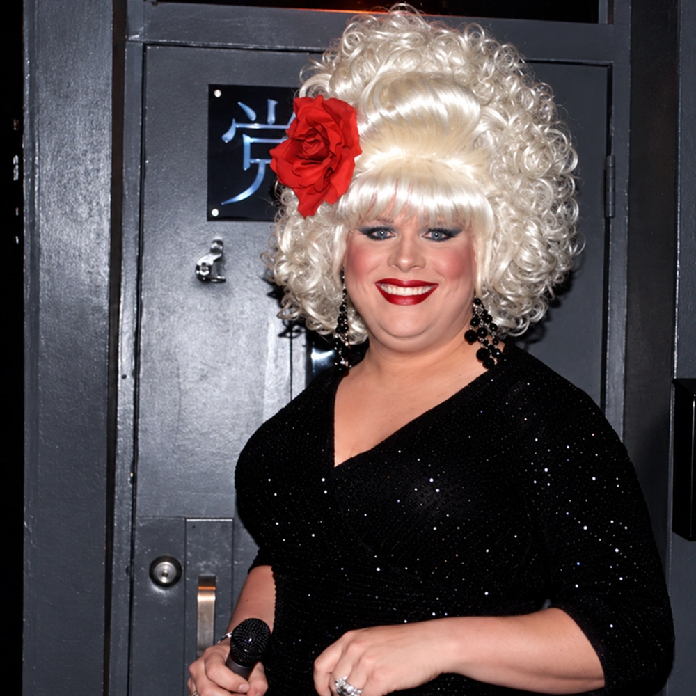 Square crop of the portrait of the drag performer with the white wig and red flower.