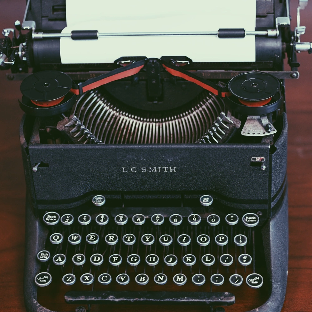 Black vintage L.C. Smith typewriter with a blank sheet of white paper in the roller and a red-and-black ribbon, round QWERTY keys.