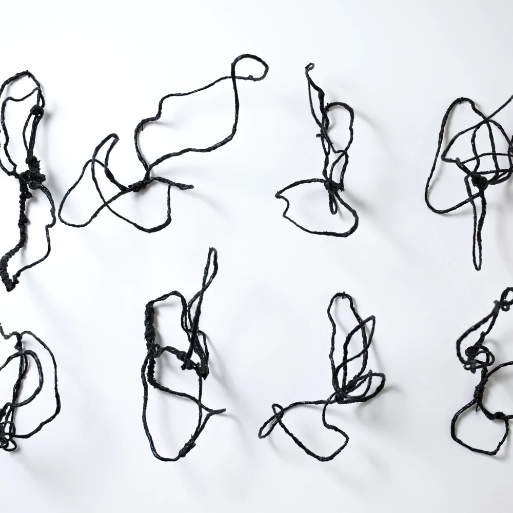 Eight black string sculptures by Robert Schatz mounted on a white gallery wall.