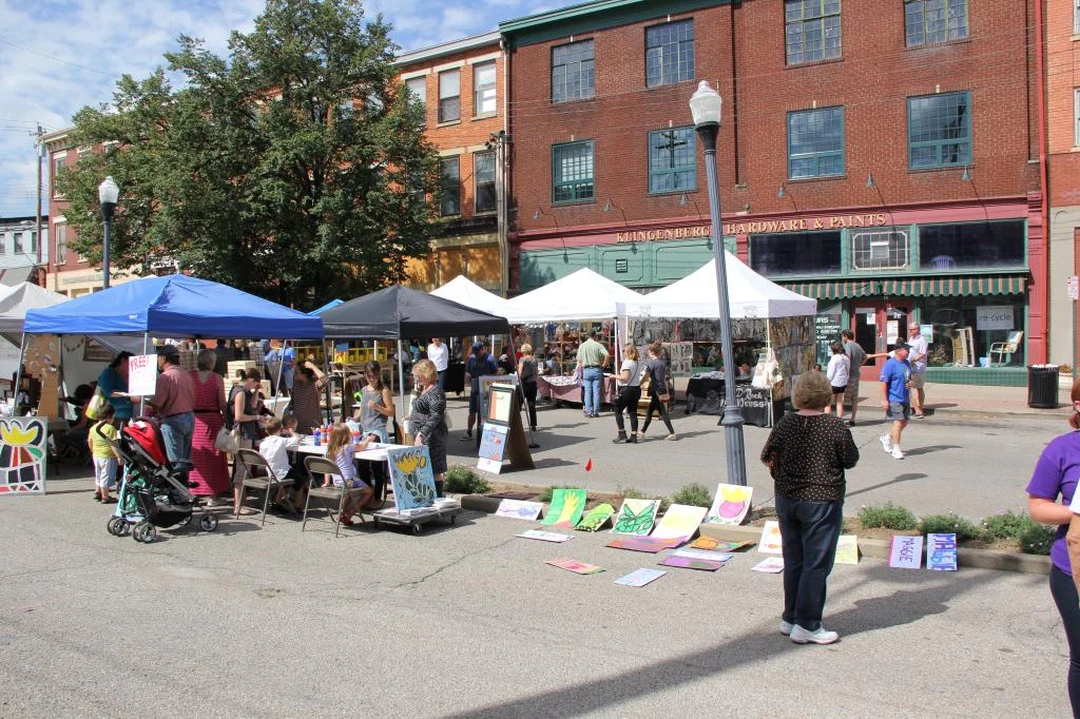 Artist booths and visitors at an outdoor street art fair in Covington, with paintings displayed on the pavement in front of brick buildings.