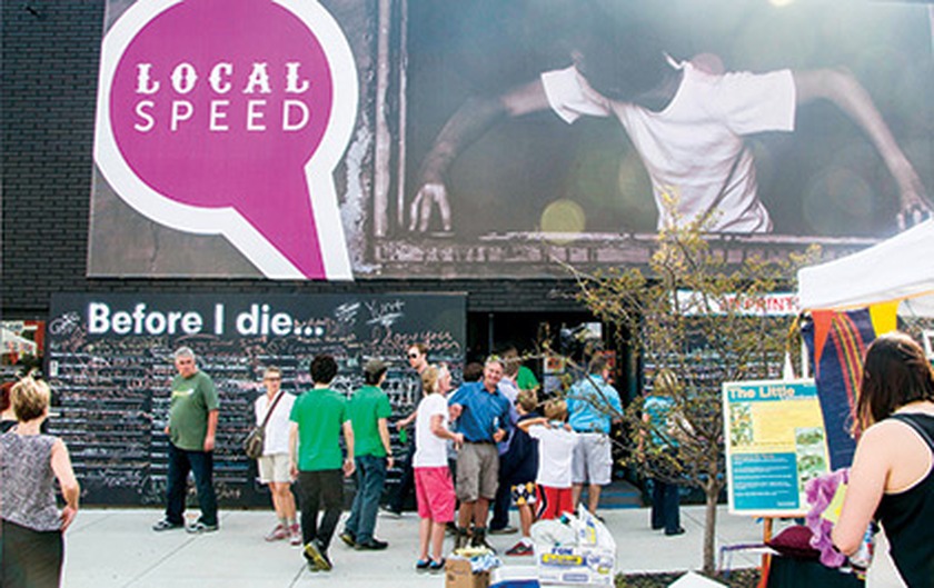 Local Speed storefront with purple speech-bubble logo sign and a “Before I die…” chalkboard wall, people gathered outside