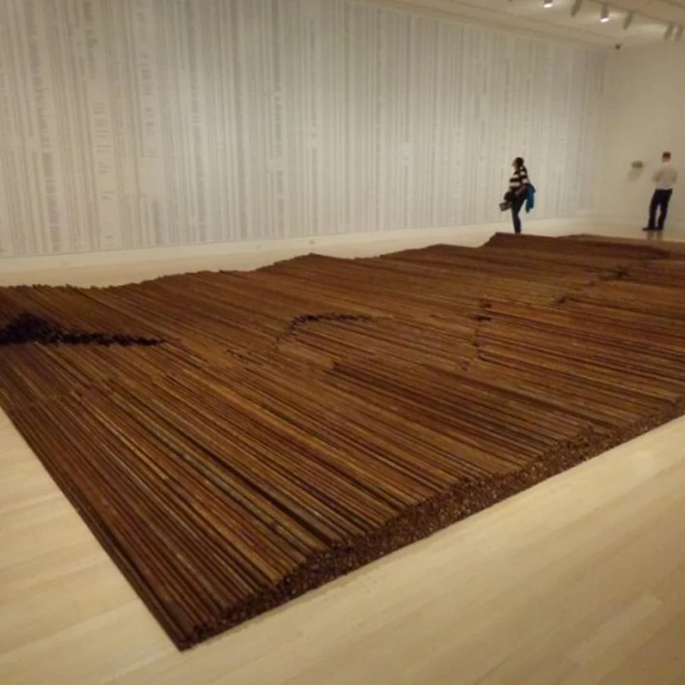 Ai Weiwei's Straight: a vast floor installation of straightened rusty rebar laid in long wave-like rows, gallery walls covered with printed lists of names, two visitors near the far wall.