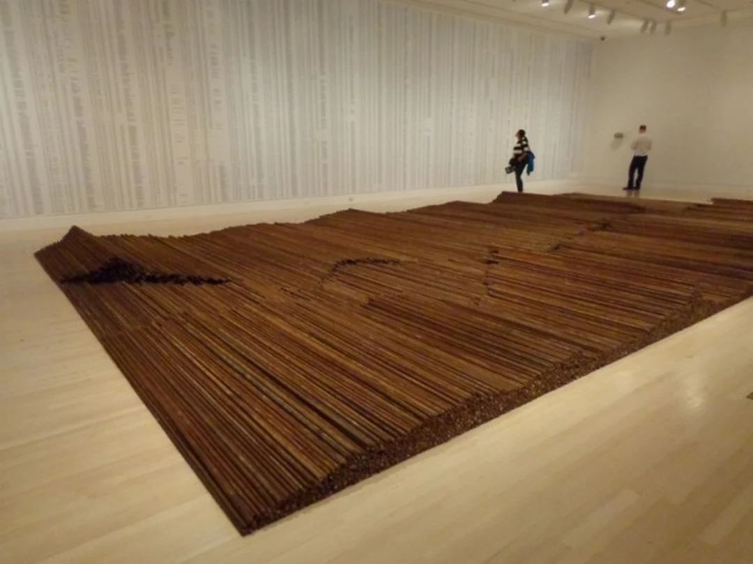 Ai Weiwei's Straight: a vast floor installation of straightened rusty rebar laid in long wave-like rows, gallery walls covered with printed lists of names, two visitors near the far wall.