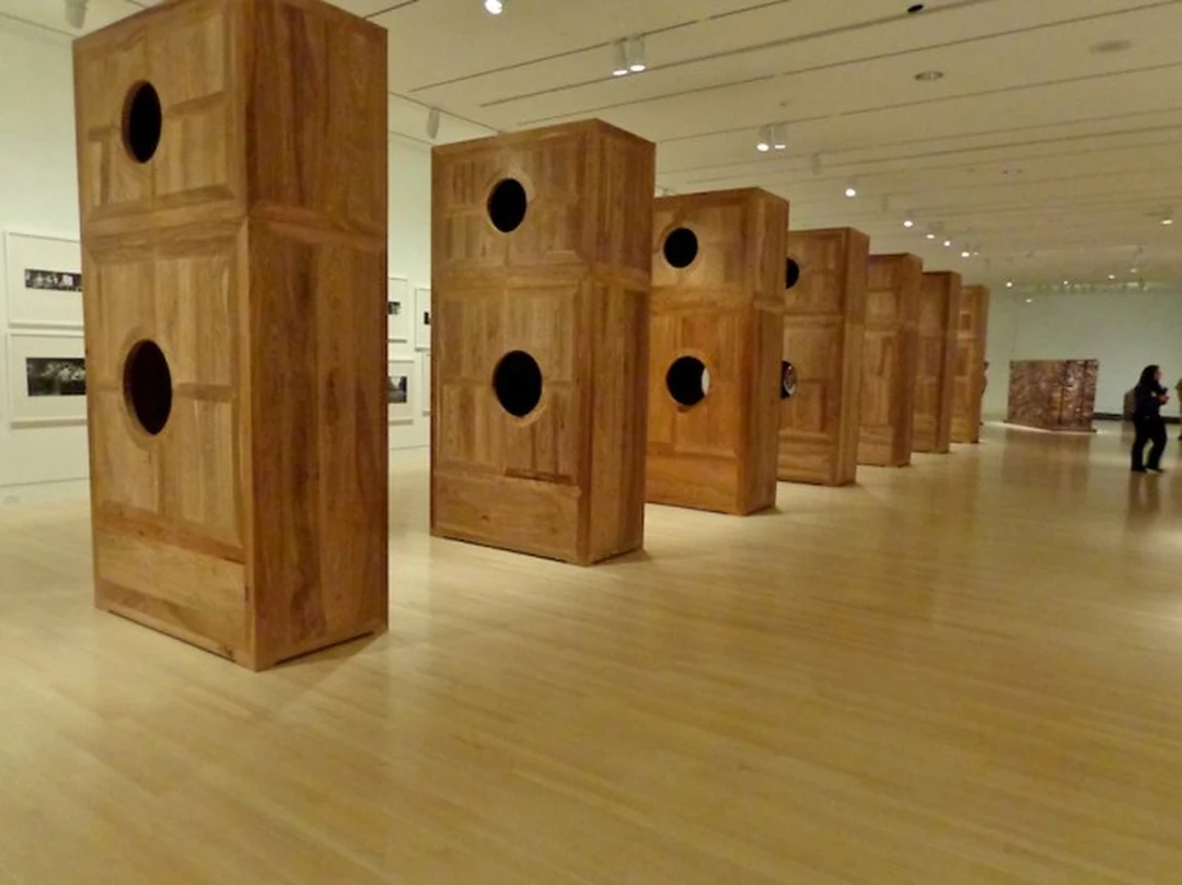 Ai Weiwei's Moon Chest: a row of tall huali-wood chests with round moon-phase cutouts receding through the gallery; the rebar field of Straight visible at right.
