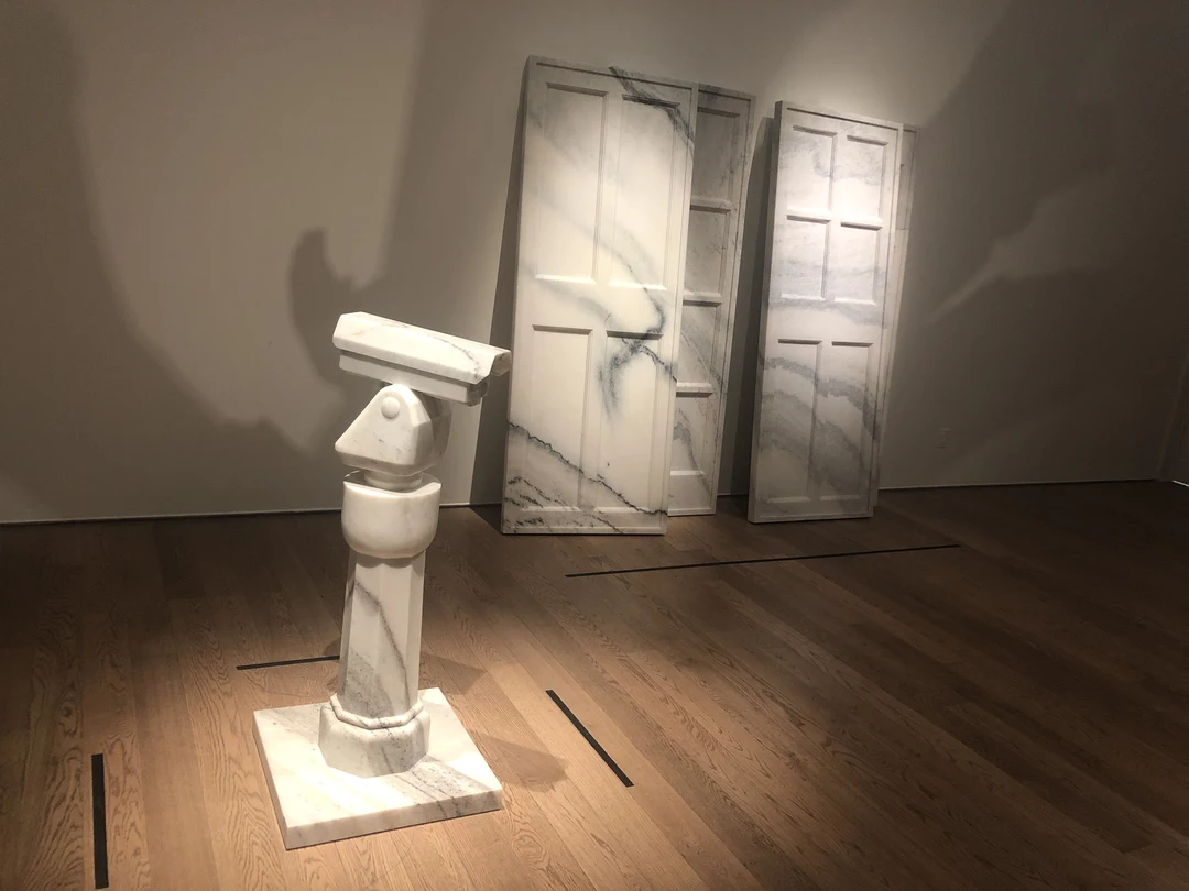 Ai Weiwei's Surveillance Camera: a white marble CCTV camera on a tall marble stand in a gallery, two marble doors leaning against the wall behind it.