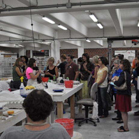 Teachers gathered around tables in an art-making workshop, with art supplies and a pottery kiln visible in the background