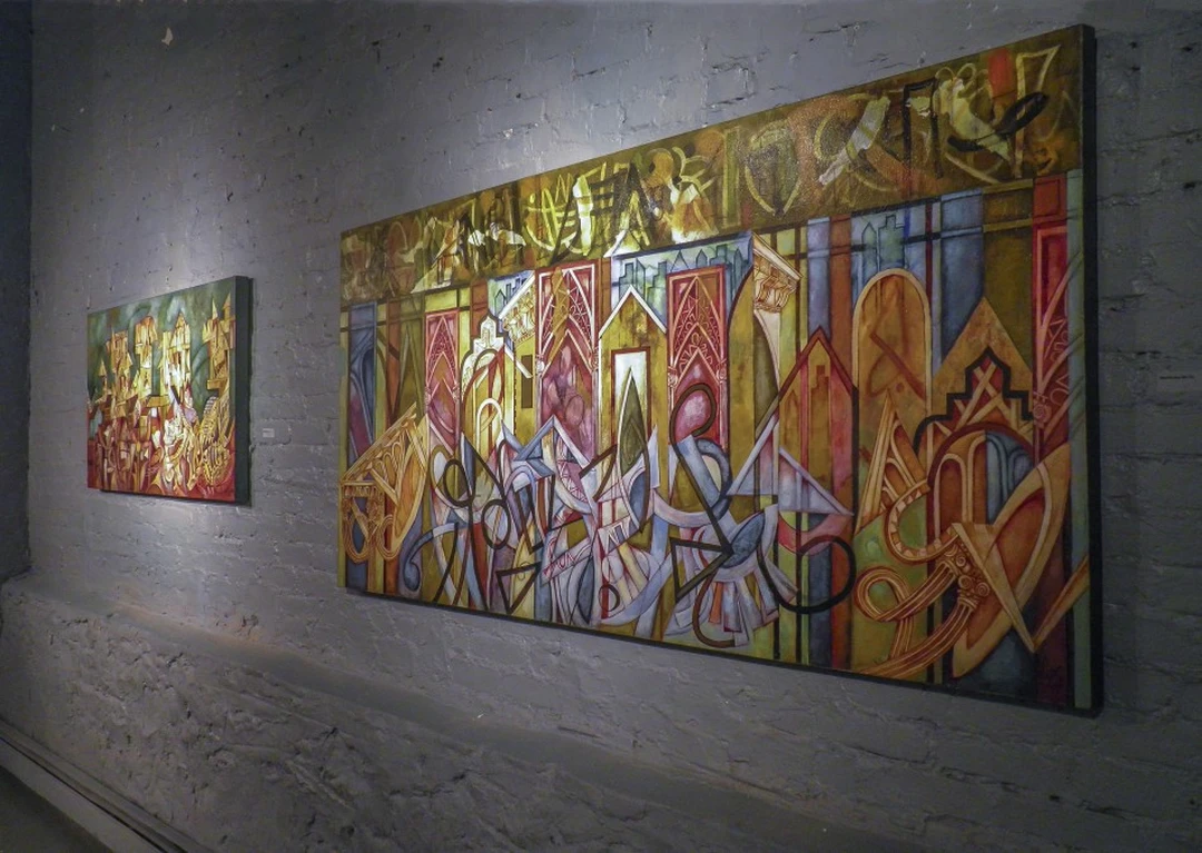 Large colorful abstract painting with architectural shapes in gold, red and blue, on a white brick gallery wall.