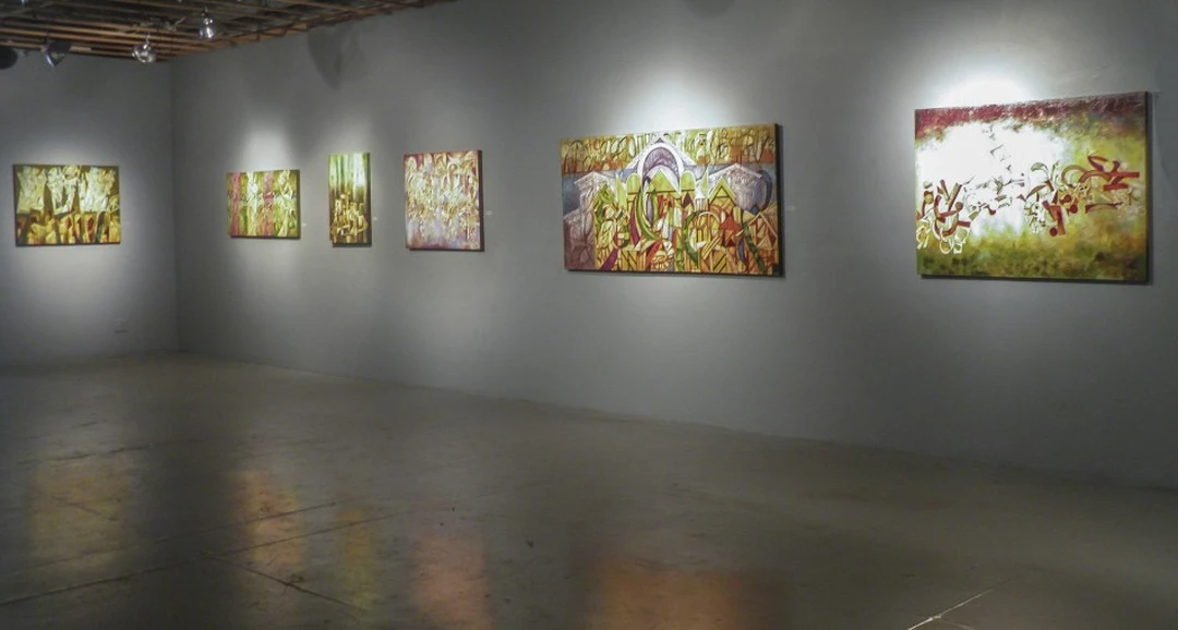 Corner view of a gallery with six colorful abstract paintings under spotlights. Photograph by Cedric Cox.