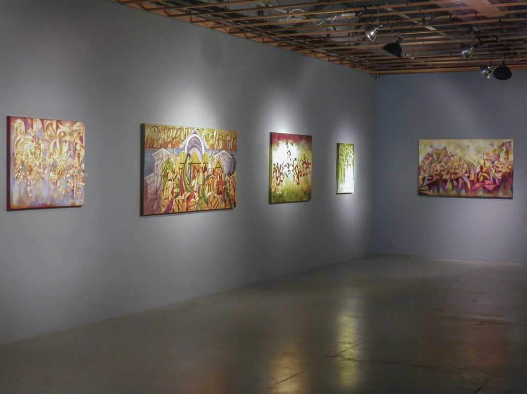 Five colorful abstract paintings on two gallery walls under track lighting. Photograph by Cedric Cox.