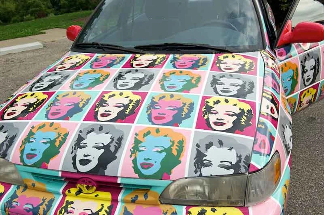 Close-up of a car hood painted with Warhol-style Marilyn Monroe faces in colorful squares.