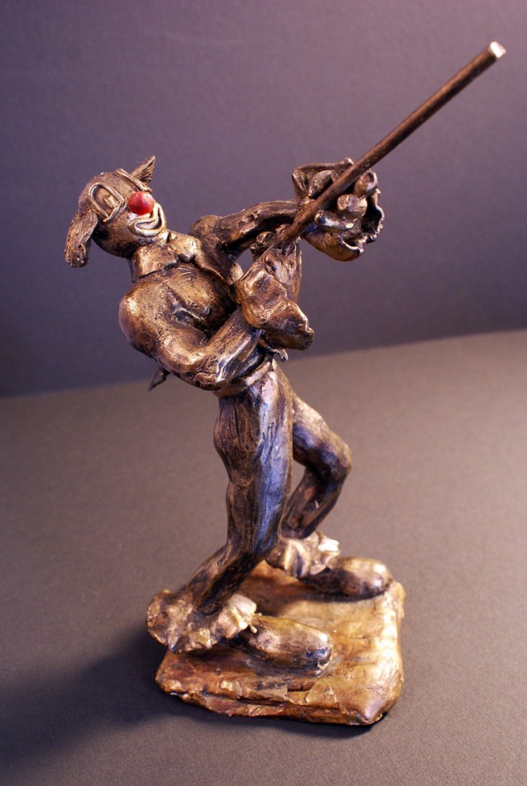 Bronze sculpture of a clown with a red nose in a dynamic pose holding a long spear diagonally.