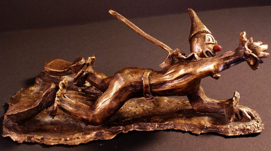 Bronze sculpture of a clown lying horizontally with an ax embedded in his back.