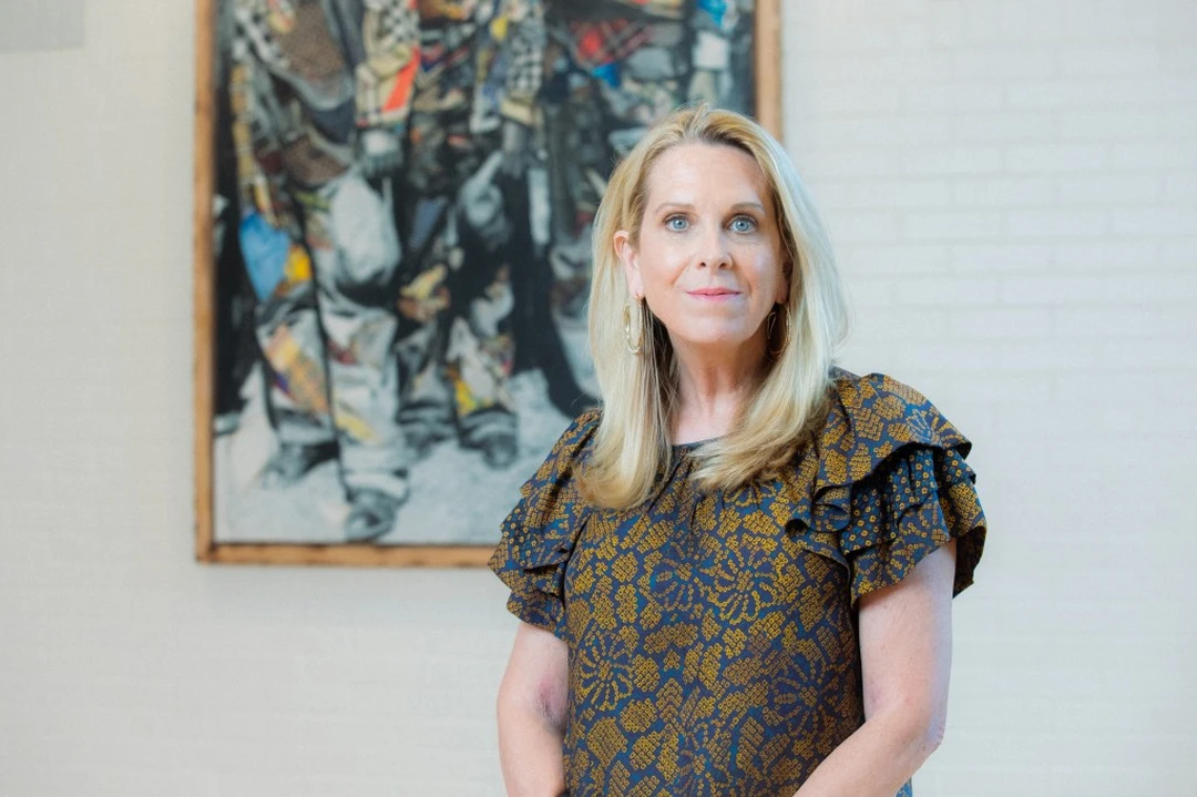 Alice Gray Stites, a blonde woman in a patterned blouse, standing in front of an artwork.