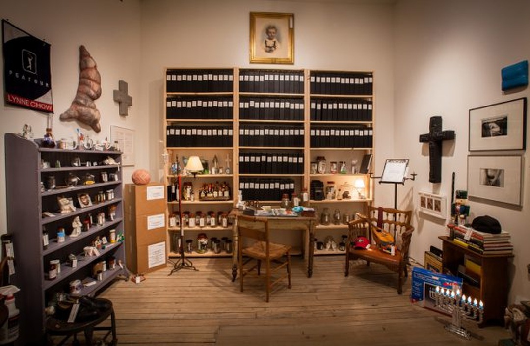 Installation view of artist Louis Zoellar Bickett's archive: shelves of labeled binders, jars, and personal objects arranged in his home studio