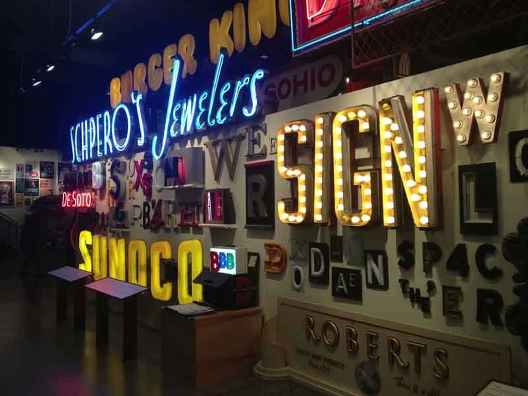 Interior of the American Sign Museum with glowing neon signs, including a large bulb-lit "SIGN".