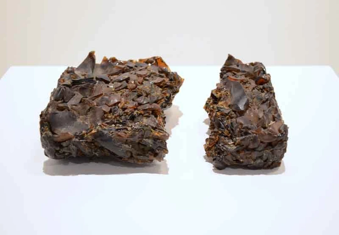 Two dark, rough sculptural chunks on a white pedestal.