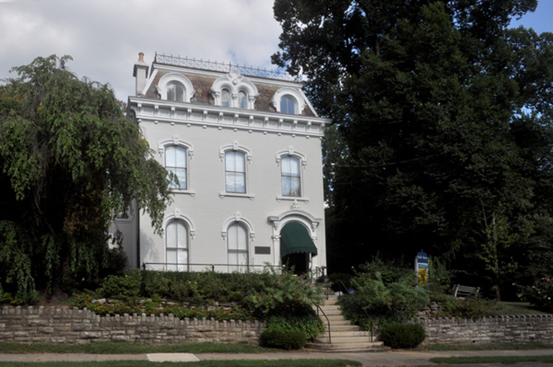 White historic building with mansard roof behind a stone wall and trees, the Baker Hunt Art & Cultural Center in Covington, Kentucky.