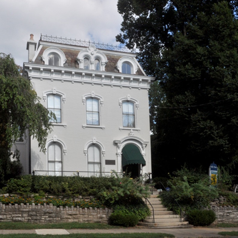 White historic building with mansard roof behind a stone wall and trees, the Baker Hunt Art & Cultural Center in Covington, Kentucky.