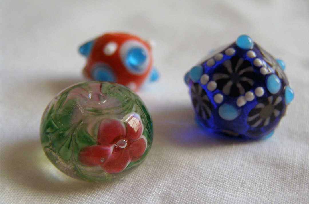 Three colorful handmade lampwork glass beads in green, red and blue on a white surface