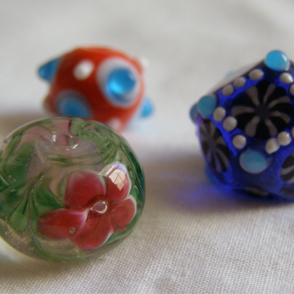 Three colorful handmade lampwork glass beads in green, red and blue on a white surface