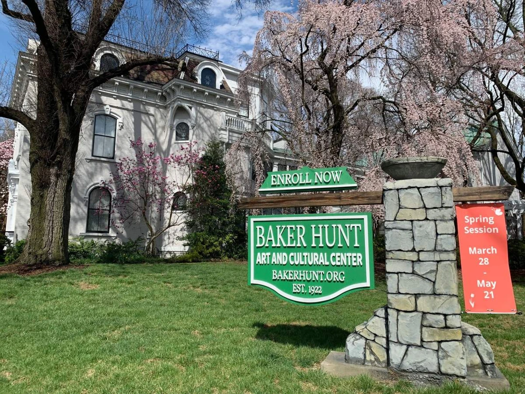Green Baker Hunt Art and Cultural Center sign with the historic white building and spring trees behind it, Covington, Kentucky.