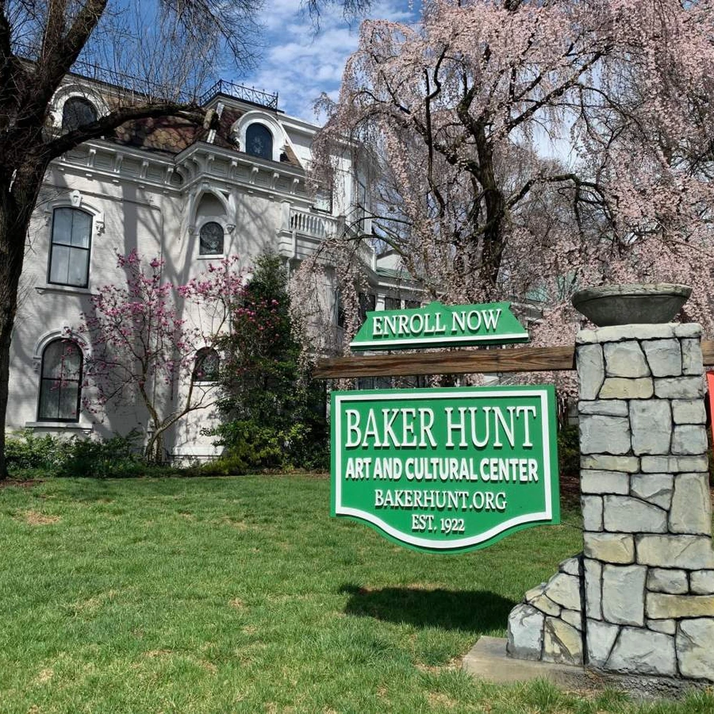 Green Baker Hunt Art and Cultural Center sign with the historic white building and spring trees behind it, Covington, Kentucky.