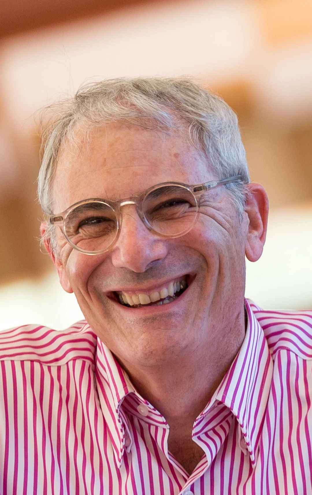 Portrait of Aaron Betsky, a smiling older man with gray hair and round glasses, wearing a pink-and-white striped shirt.
