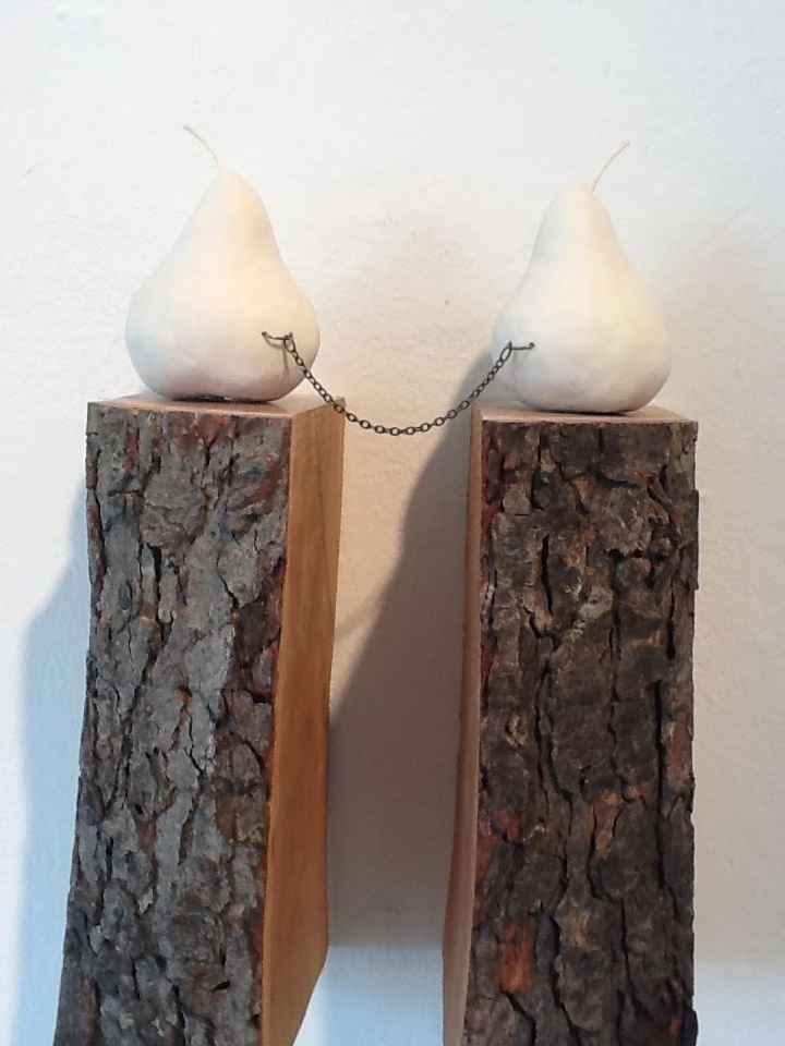 Two matte-white porcelain pears on bark-covered wooden blocks, joined by a short metal chain strung between rings.
