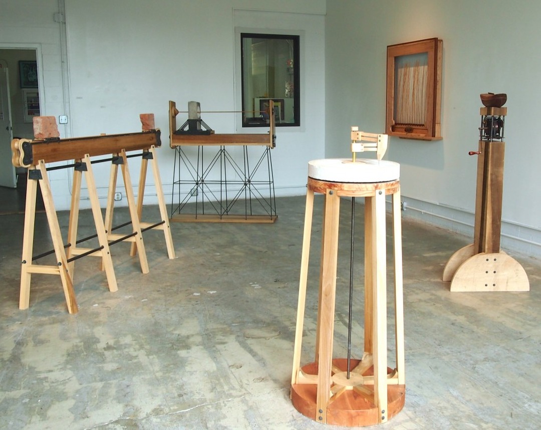 Installation view of the exhibition at Brazee Studios: several wooden kinetic sculptures, including sawhorse structures with bricks, a round table and a tall column.